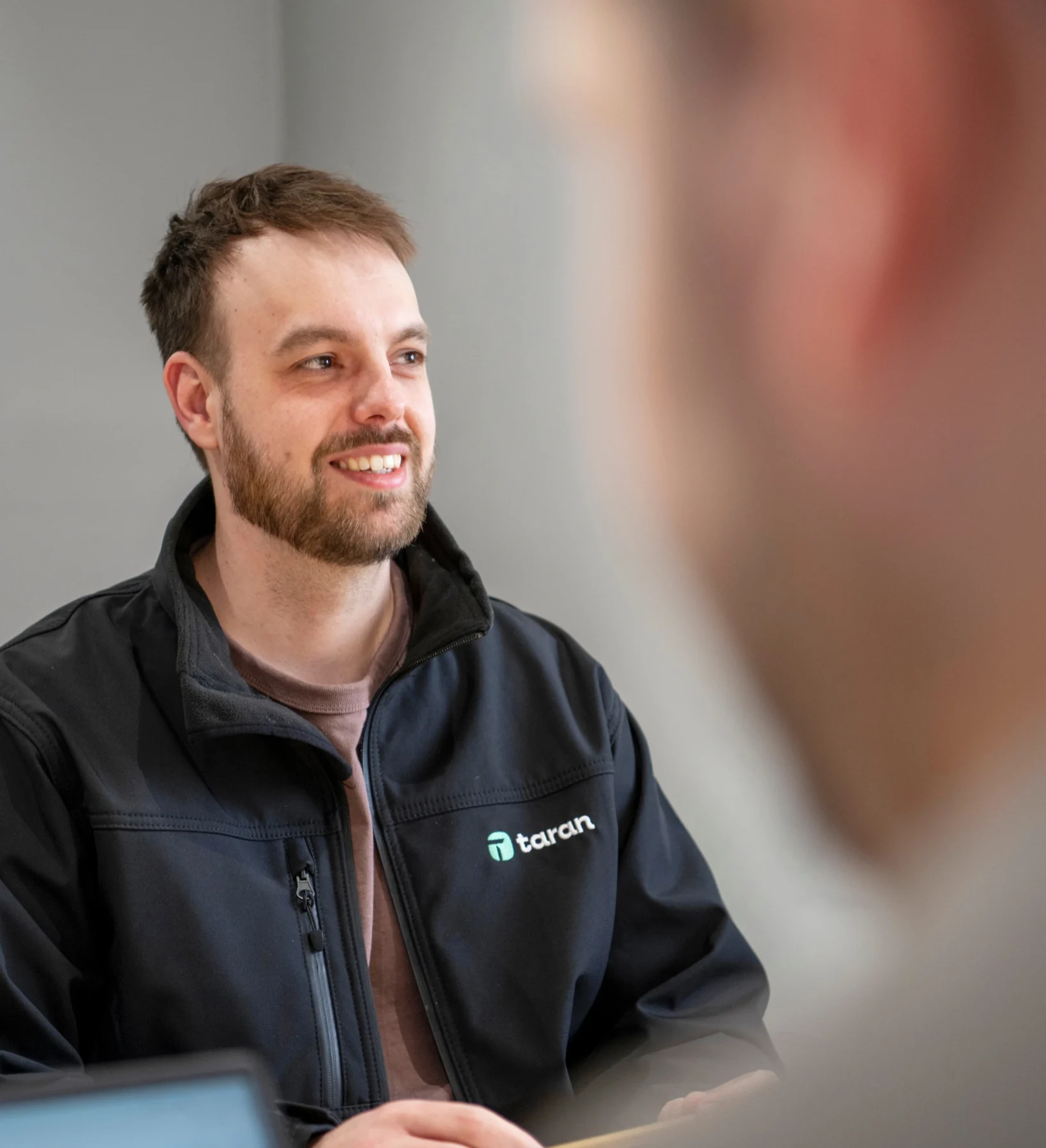 Taran IT consultant smiling during a meeting with a colleague in the office.